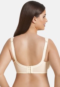 Beige bra with a smooth fabric, wide straps, and a four-hook back closure. Features a seamless design and a soft, stretchy texture.
