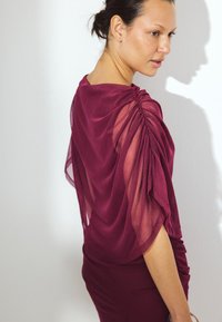 Bordeaux top met doorschijnende, gedrapeerde mouwen en gerimpelde details op de schouders. Soepele textuur en aansluitende silhouet.