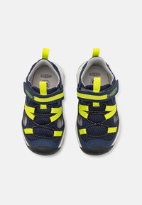 Sapatos em rede azuis com correias em amarelo néon, fecho em Velcro, palmilha acolchoada e sola de borracha texturizada para aderência. Design leve para conforto.