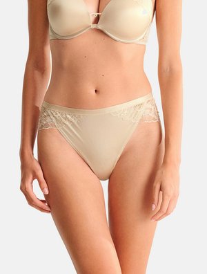 Soutien-gorge beige et culotte assortie bordée de dentelle portés par une femme, montrant le torse et le haut des cuisses sur un fond clair uni.