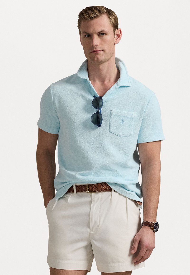Lichtblauw terry stof polo shirt met een borstzak, korte mouwen en een kraag; gecombineerd met crèmekleurige shorts en een bruine gevlochten riem.