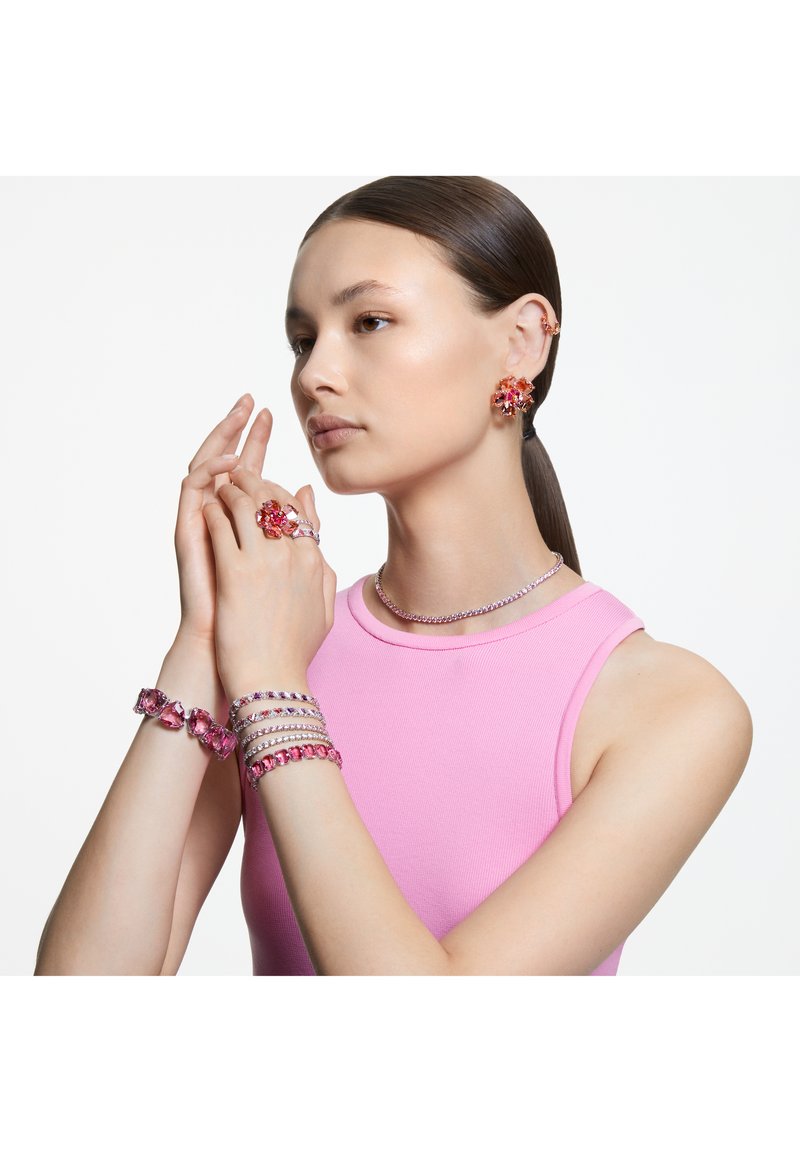 Coleção de joias com brincos de cristal rosa, pulseiras e anel; detalhes em prata, design floral e texturas suaves, usados com uma blusa rosa.