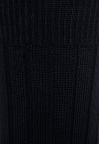 Strickkleidungsstück in dunklem Marineblau; verfügt über eine vertikale Rippstruktur mit kontrastierenden glatten Abschnitten. Weiches, flexibles Material; keine sichtbaren Beschläge.