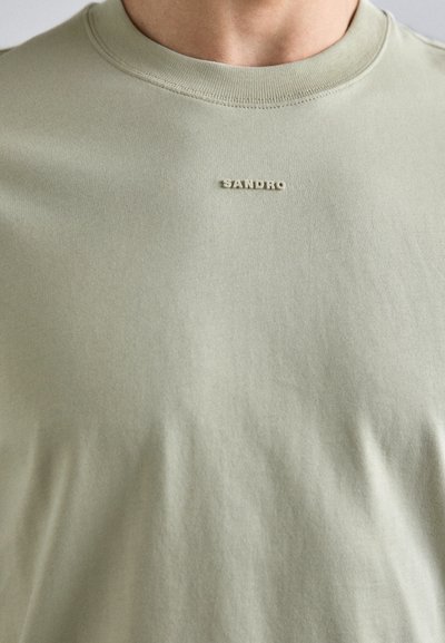 Hele roheline puuvillane T-särk, millel on ümar kaelus, pehme tekstuur ja ees väike reljeefne "SANDRO" logo.