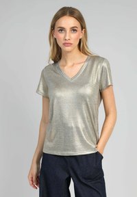 T-shirt à col V en métal doré à manches courtes, avec une texture lisse et une coupe décontractée, associé à un pantalon en denim sombre.