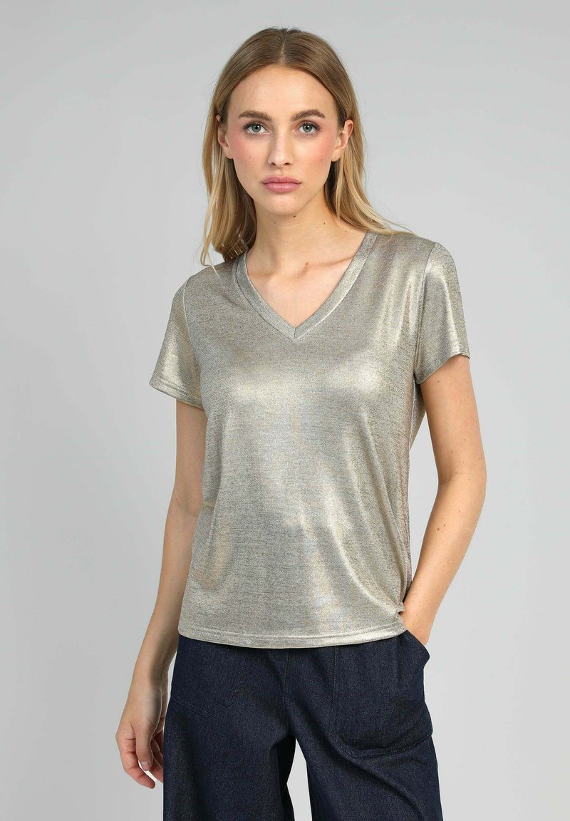 T-shirt à col V en métal doré à manches courtes, avec une texture lisse et une coupe décontractée, associé à un pantalon en denim sombre.