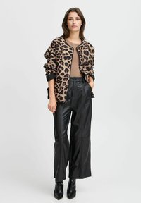 Cardigan a stampa leopardo, strutturato, con rifiniture nere, indossato sopra una maglietta marrone. Pantaloni in pelle neri a vita alta e scarpe con tacco a punta.