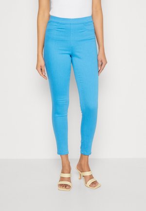 Blå elastiska denimleggings med hög midja, med två framfickor och smal passform, ihop med ljusgula klacksandaler.