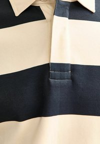 Koszulka polo w poziome paski w kolorze granatowym i kremowym. Wykonana z bawełny, posiada kołnierzyk oraz trzy guziki. Gładka tekstura.