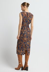 Blå- och brunt blommönstrad klänning med åtsittande midja, axelärmar, sprund bak och knälång längd, i kombination med bruna klackboots.