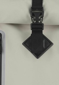 Material del zaino impermeabile grigio chiaro con fibbia e cinghia in plastica nera, dotato di un accento a forma di diamante e superficie testurizzata.