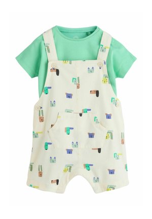 Grünes kurzärmeliges Hemd kombiniert mit cremefarbenen Latzhosen, die bunte Cartoon-Tiergesichter und eine Fronttasche zeigen.