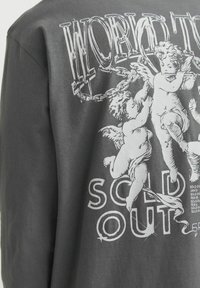 Graues Baumwoll-T-Shirt mit einem Grafikenprint von zwei Cherubinen, die in Ketten verwoben sind, und dem deutlich hervorgehobenen Text "AUSVERKAUFT" darunter.