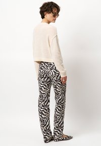 Gekürzter beiger Wollpullover kombiniert mit hoch taillierten Hosen in einem schwarz-creamfarbenen wellenförmigen Muster. Modell trägt schicke Ballerinas.