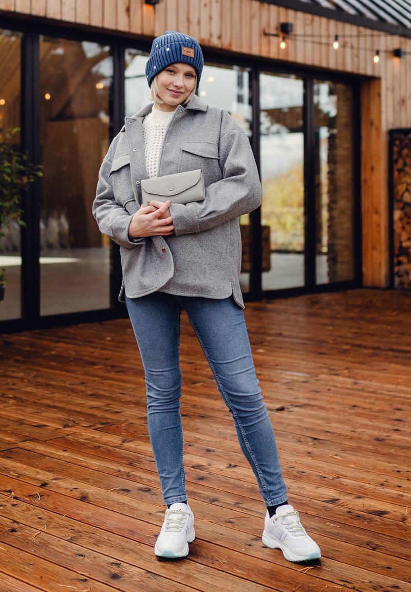 Gray wool shirt jacket over a white knitted sweater, blue jeans, and white sneakers with mint accents. Wearing a navy beanie and holding a gray clutch.