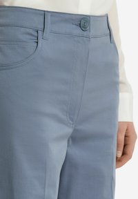 Ljusblå byxor i slät tygkvalitet. Har knappstängning, bältesöglor och sidfickor med subtila sömnadsdetaljer.