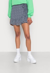 Marineblaues Blumenkleid mit Rüsche am Saum, aus leichtem Stoff, kombiniert mit weißen klobigen Sneakers und Kniestrümpfen.