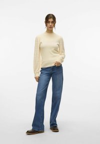 Lichtbeige langemouwen top met getextureerde mouwen, gecombineerd met blauwe wijde jeans en bruine enkellaarsjes. Eenvoudig, strak ontwerp.