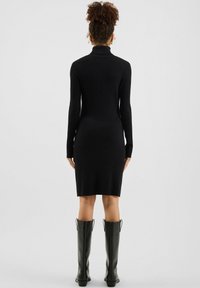 Schwarzes, geripptes Strickkleid mit Rollkragen, figurbetonte Silhouette, mittellange Länge bis zur Mitte des Oberschenkels, lange Ärmel, kombiniert mit kniehohen schwarzen Stiefeln.