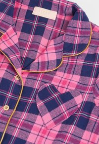 Różowo-granatowa koszula do piżamy w kratę z złotą lamówką, drewnianymi guzikami i kieszenią na piersi, złożona tak, aby wyeksponować kołnierz i metkę.