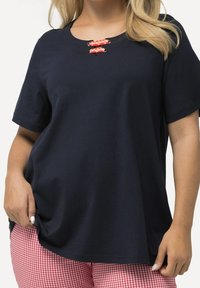 Tmavě modrý krátký top s výstřihem do oblouku a dvěma dekorativními červenobílými kostkovanými akcenty na prsou. Hladká textura látky.