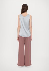 Lichtblauw satijnen tanktop met een V-hals, gecombineerd met brede, hooglopende broek in stofroze met een gladde textuur en een nette afwerking aan de onderkant.