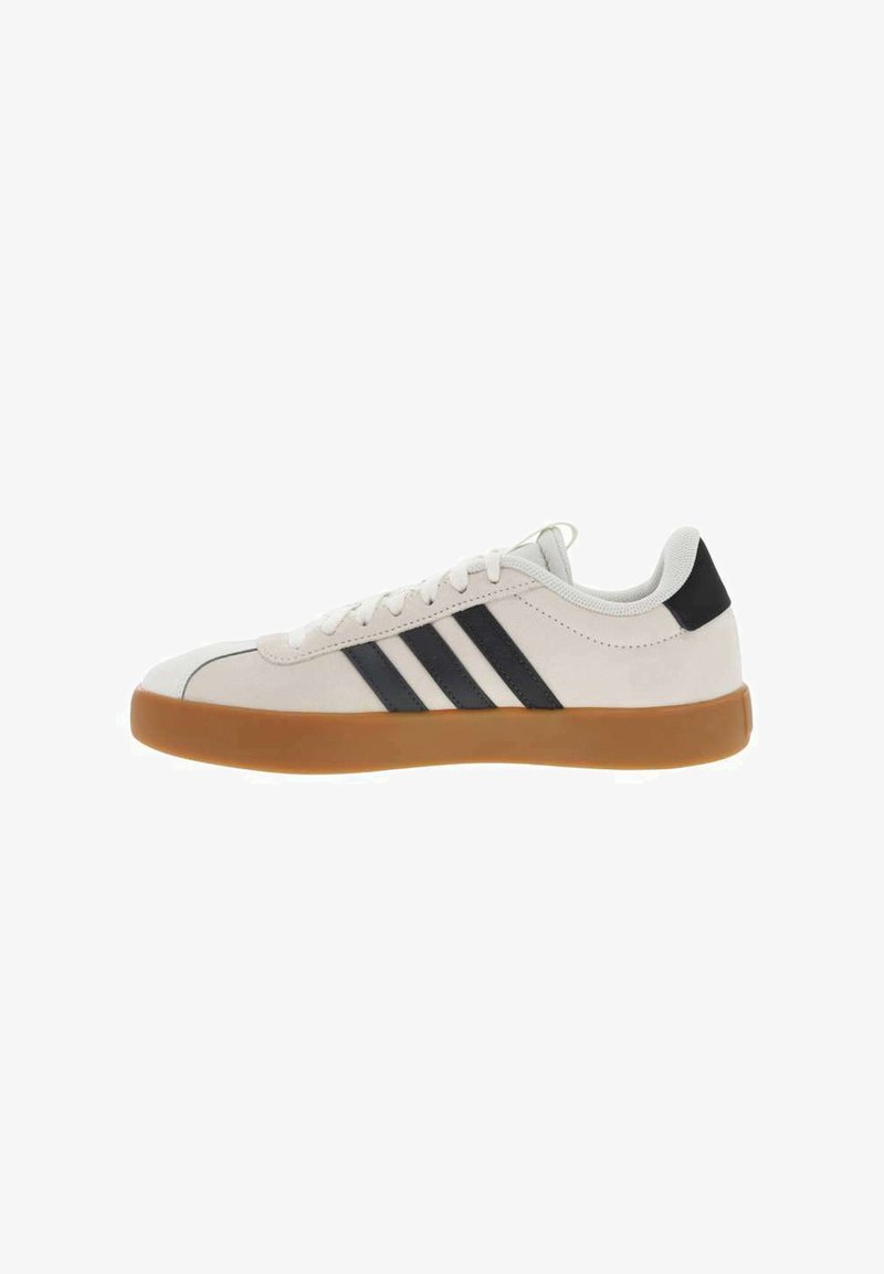 Zapatilla blanca con tres rayas negras, suela de goma, puntera redondeada y parte superior de textil suave. Cuenta con un cuello acolchado para mayor comodidad.