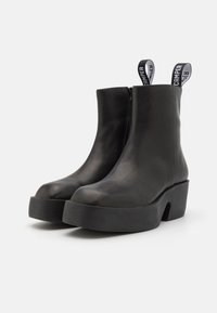 Black leather ankle boots with a rounded toe, a chunky platform sole, and two fabric pull tabs with branding at the back.