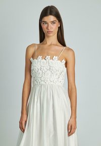 Witte jurk met een kant bodice met florale patronen, dunne schouderbanden en een vloeiende, gestructureerde rok.