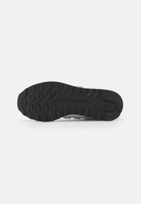 Black textured rubber sole of a sneaker with tread patterns and a small "NB" logo near the heel on a white background.