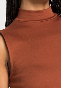 Haut sans manches couleur rouille avec un col haut, fabriqué en tissu côtelé, présentant une texture lisse et une coupe ajustée.