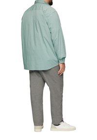 Jasnozielona koszula z długim rękawem w mały wzór w kropki, zestawiona z szarymi spodniami o tapered cut i białymi snekerami, widok z tyłu.