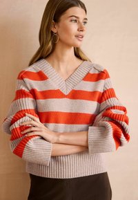 V-hals sweater med horisontale striber i grå og lysende orange. Strikstruktur med ribbede manchetter og kant, lidt afslappet pasform.