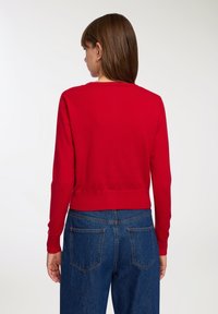 Maglione rosso lavorato a maglia con maniche lunghe, scollo rotondo e orlo a coste, abbinato a jeans in denim blu con tasche posteriori.