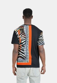 T-shirt nero e arancione a fantasia con stampa animale audace sul lato sinistro e dettagli decorativi, dal taglio morbido e con maniche corte.