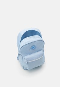 Ljust blå ryggsäck i mjukt material med en rund logotyp, framficka med dragkedja och två justerbara axelremmar. Rundad design upptill.