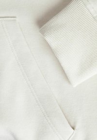 Sweatshirt beige chiaro con polsini a coste e tasca frontale. Il tessuto testurizzato appare morbido con dettagli di cucitura ben rifiniti.