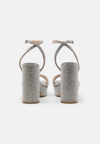 Silberne High-Heels-Sandalen mit einem funkelnden, mit Strass besetzten Obermaterial, dicken Blockabsätzen und überkreuzten Knöchelriemen.