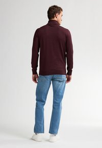Burgunderfarbener Rollkragenpullover mit gerippten Bündchen und Saum, kombiniert mit hellblauen geraden Jeans und weißen Sneakers.