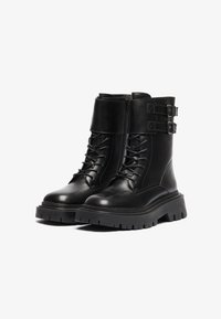 Botas de cuero negro hasta el tobillo con cierre de cordones en la parte delantera, diseño de tobillo alto, dos hebillas ajustables y suela de goma gruesa con dibujo profundo.