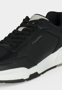 Μαύρο και άσπρο αθλητικό παπούτσι Calvin Klein με κορδόνια μπροστά και υφή στη σόλα, που δείχνει το λογότυπο στο πλάι και επενδεδυμένο γύρω από τον αστράγαλο.