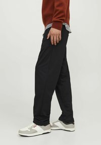 Pantaloni neri in morbido tessuto, con un design a gamba dritta. Abbinati a sneakers bianche e grigie, e un maglione color ruggine indossato sopra una camicia a righe.