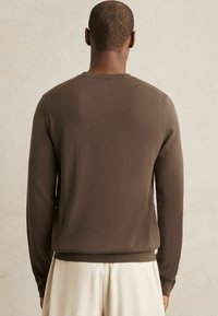 Brauner Langarm-Pullover aus weichem Material mit Rundhalsausschnitt und gerippten Bündchen, von hinten gezeigt. Strukturierter Stoffabschluss.