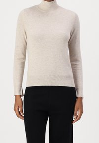 Beige polotröja i mjukt stickat material, med långa ärmar och ribbad nederkant. Designad med sidospjälor för rörelsefrihet.