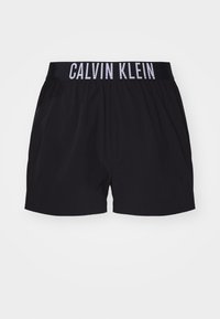 Shorts noirs avec une taille élastique arborant le logo "CALVIN KLEIN" en blanc. Fabriqués en tissu léger, avec une texture lisse et une longueur jusqu'au genou.