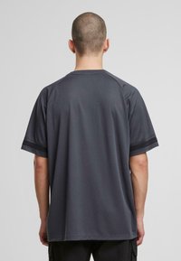 Hallhargi lühikeste varrukatega särk, mis on valmistatud hingavast kangast ja on siledat tekstuuri. Omab raglan-varsuseid ja musti aktsente mansettidel.