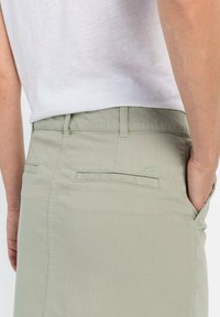 Helle grüne Hose mit glatter Textur, Gesäßtaschen mit sauberem Finish und einem dezenten Logo nahe dem Bund.