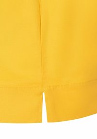 Gelbes Baumwollgewebe mit geradem Schnitt, das einen kleinen Schlitz am Saum hat. Glatte Textur und gleichmäßige Nähdetails.