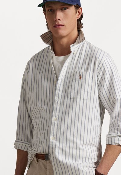 White striped button-up shirt made of lightweight fabric, featuring a chest pocket and embroidered logo. Rolled sleeves and casual collar.