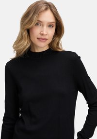 Czarny sweter z długim rękawem i wysokim, teksturowanym dekoltem z małymi ozdobami. Gładka tkanina, dopasowany krój, minimalistyczny design.